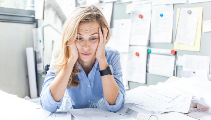 A stressed woman surrounded with paperwork with her hands on her head A stressed woman surrounded with paperwork with her hands on her head