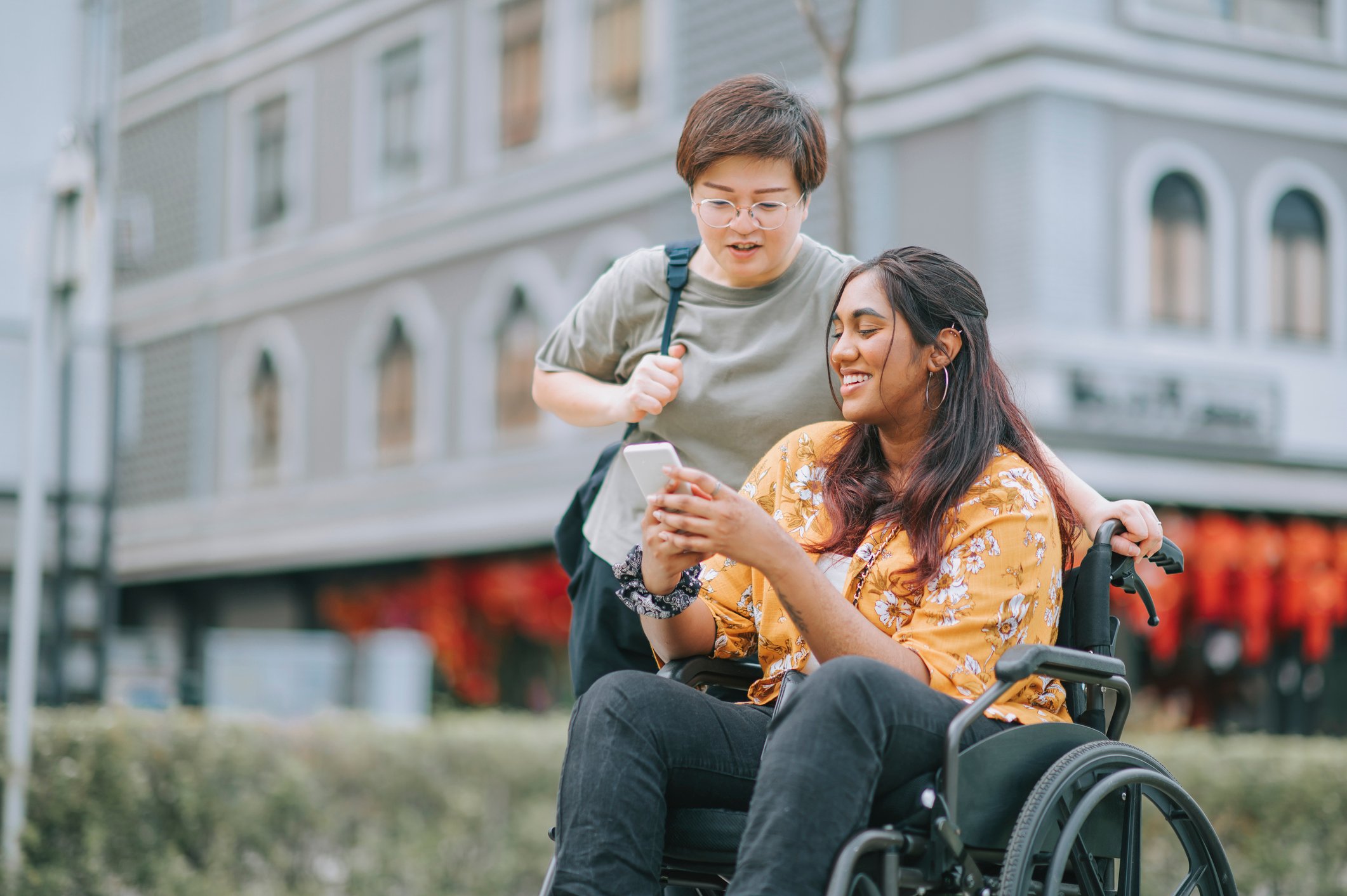 two female looking at a phone and one female is sitting on wheel chair